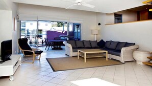 A modern living room with a sofa, coffee table, TV, and a dining area with chairs and a table. - Beachdaze at Hyams Beach (Hyams Beach)