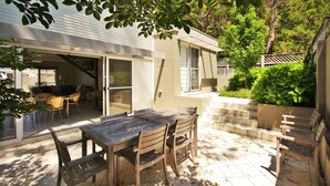 An outdoor patio with a wooden table and chairs, a sliding glass door leading to an interior space, and a staircase leading to a second level. - Beachdaze at Hyams Beach (Hyams Beach)