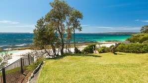 A coastal view with a grassy area, trees, and a beach. - Bimbadgen at Hyams Beach (HYAMS BEACH)