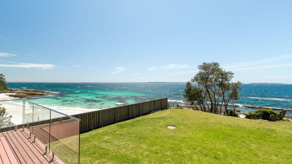 Una terraza moderna al aire libre con barandilla de vidrio, con vista a una playa y el océano.
