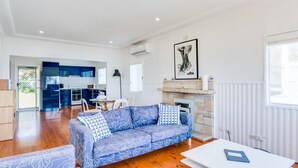 A spacious living room with a blue patterned sofa, a dining area with a white table, and a kitchen with blue cabinets. - Bimbadgen at Hyams Beach (HYAMS BEACH)
