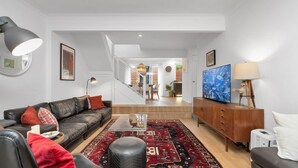 Een moderne woonkamer met een leren bank, een bijzettafeltje en een televisie op een houten kast. Een trap leidt naar een verdieping daarboven.