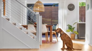 Een modern interieur met een trap, een eethoek en een hond die bij een raam zit.