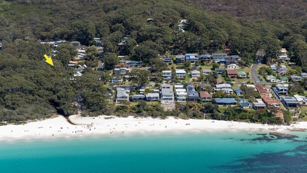 Luchtbeeld van een kustgebied met woningen, een strand en een beboste heuvel.
