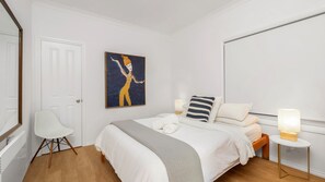 Ett hotellrum med en säng, en stol, en tavla och sänglampor.