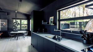 A modern kitchen with a large window, dark cabinetry, and a dining area with a table and chairs.