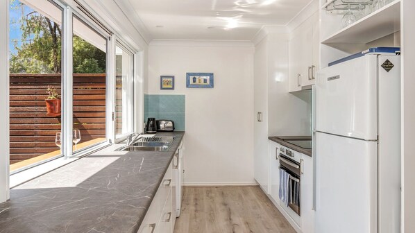 Una cocina compacta con horno empotrado, refrigerador y cafetera.