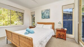 Une chambre à coucher avec un grand lit, une table de chevet, une chaise en osier et un tableau accroché au mur.