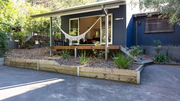 A modern house with a hammock on the porch, wooden deck, and a garden with various plants. - Boathouse 1, Hyams Beach (Hyams Beach)