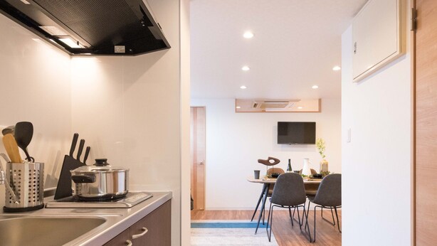 A modern kitchen with a stainless steel sink, wooden cabinets, and a built-in stove. There is a dining area with a table and chairs, and a TV mounted on the wall. - TORA HOTEL Skytree B (Tokyo)