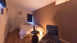 A hotel room with a bed, a chair, a small table with a lamp, and a wall-mounted air purifier. - TORA HOTEL Skytree B (Tokyo)