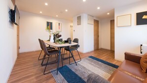 A modern living room with a brown leather sofa, a dining area with a table and chairs, and a TV mounted on the wall. - TORA HOTEL Skytree B (Tokyo)
