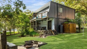 A modern two-story house with a balcony, surrounded by a well-maintained garden and a small outdoor fire pit.