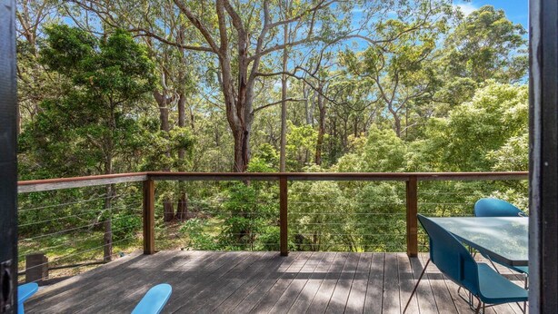 A wooden deck with a railing, overlooking a forested area with trees and greenery.