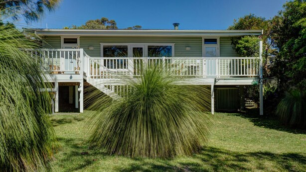 A two-story house with a covered porch, a staircase leading to the upper level, and a well-maintained lawn. - Calypso's Cottage at Hyams Beach (Hyams Beach)