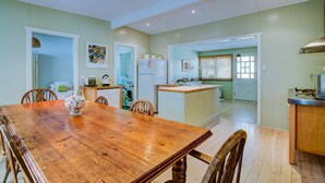A spacious dining area with a wooden table and chairs, a kitchen with a refrigerator and a microwave, and a small island with a sink. - Calypso's Cottage at Hyams Beach (Hyams Beach)