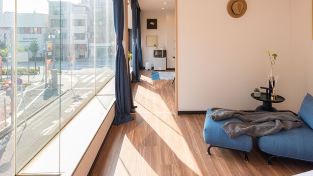 Una habitación de hotel moderna con un ventanal amplio, un sofá, una pequeña mesa con un florero y vistas a la ciudad.