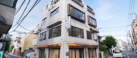 A multi-story building with a tiled facade, a visible art studio on the ground floor, and a parked car on the street.