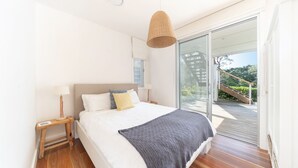Un dormitorio moderno con una cama grande, una mesita de noche de madera, una lámpara de noche y vistas a una terraza y escalera de madera.