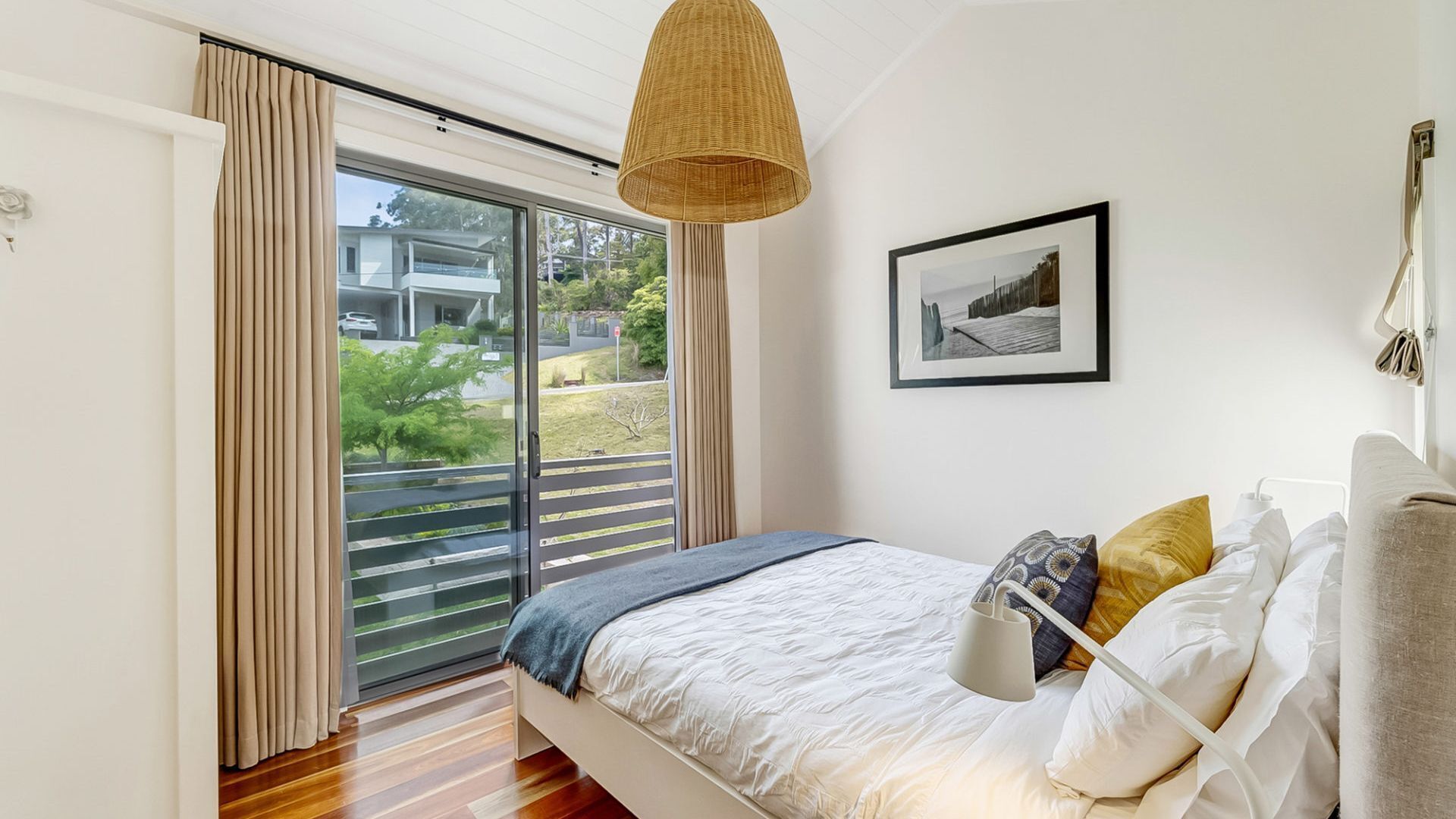 A bedroom with a bed, a large window with curtains, a hanging light fixture, and a framed picture on the wall.