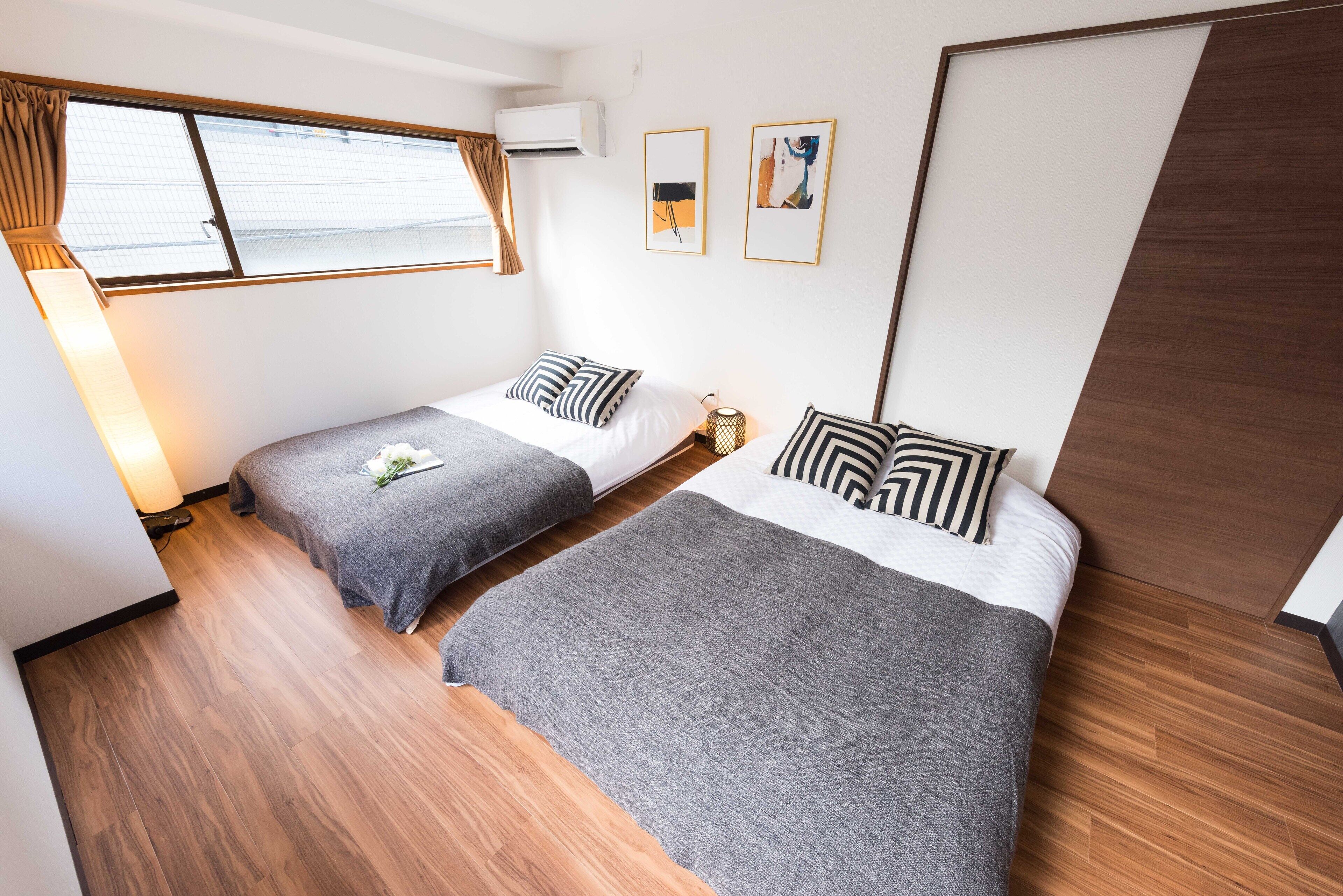 Een slaapkamer met twee bedden, een raam met gordijnen en een kunstwerk in een lijst aan de muur.