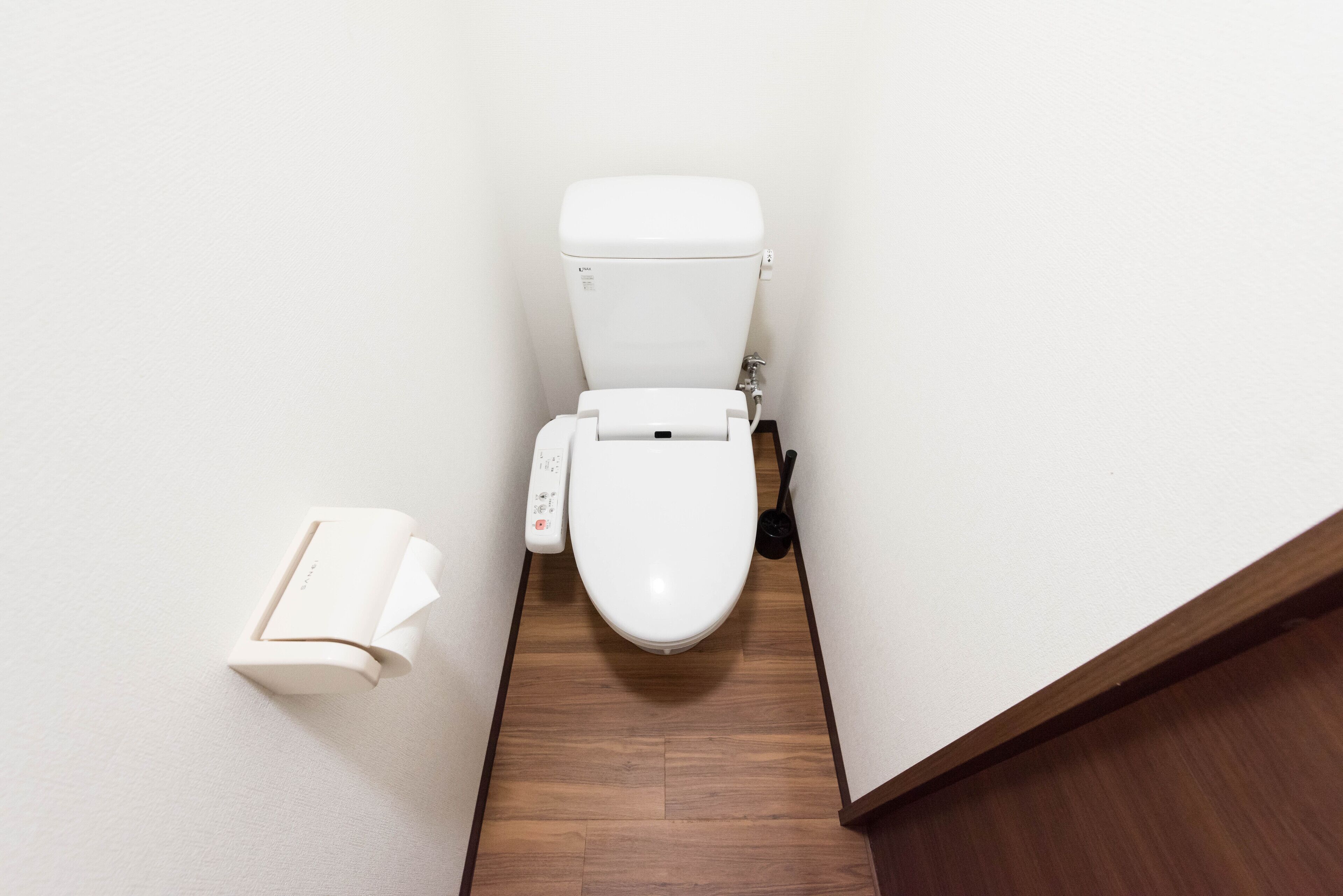 A toilet with a control panel, a toilet paper holder, and a wooden floor.