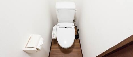 Un inodoro con un panel de control, un dispensador de papel higiénico y suelo de madera.