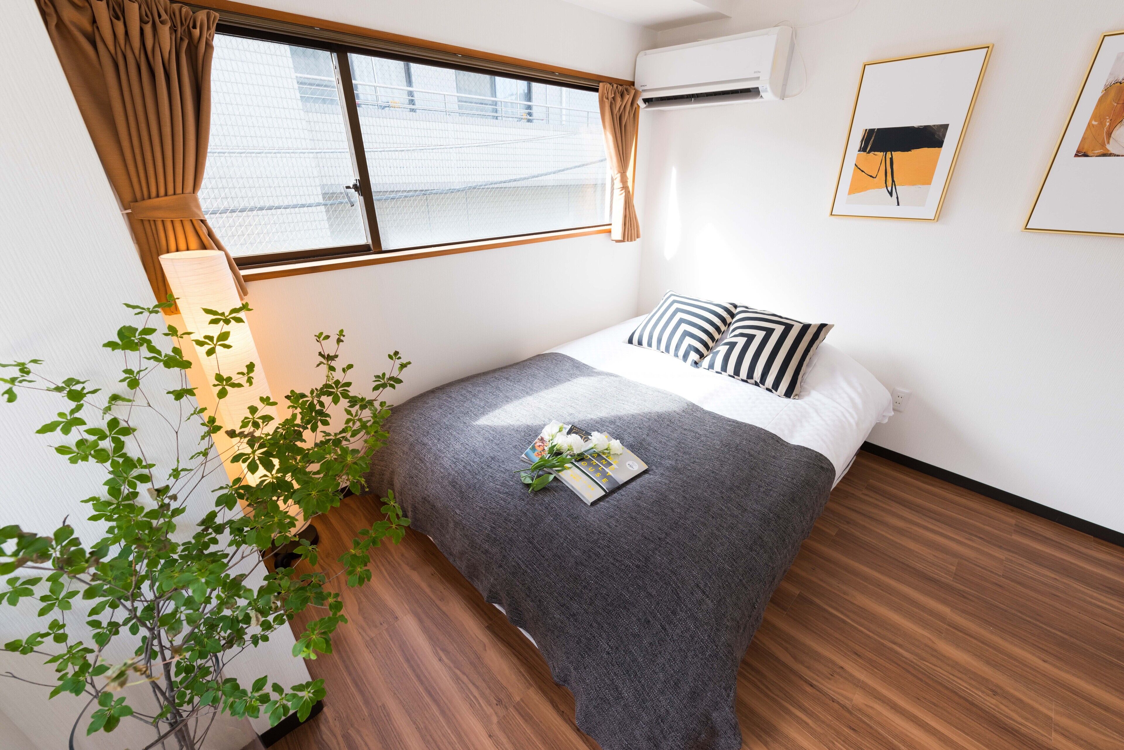 A neatly arranged bedroom with a bed, a potted plant, and a window with curtains.