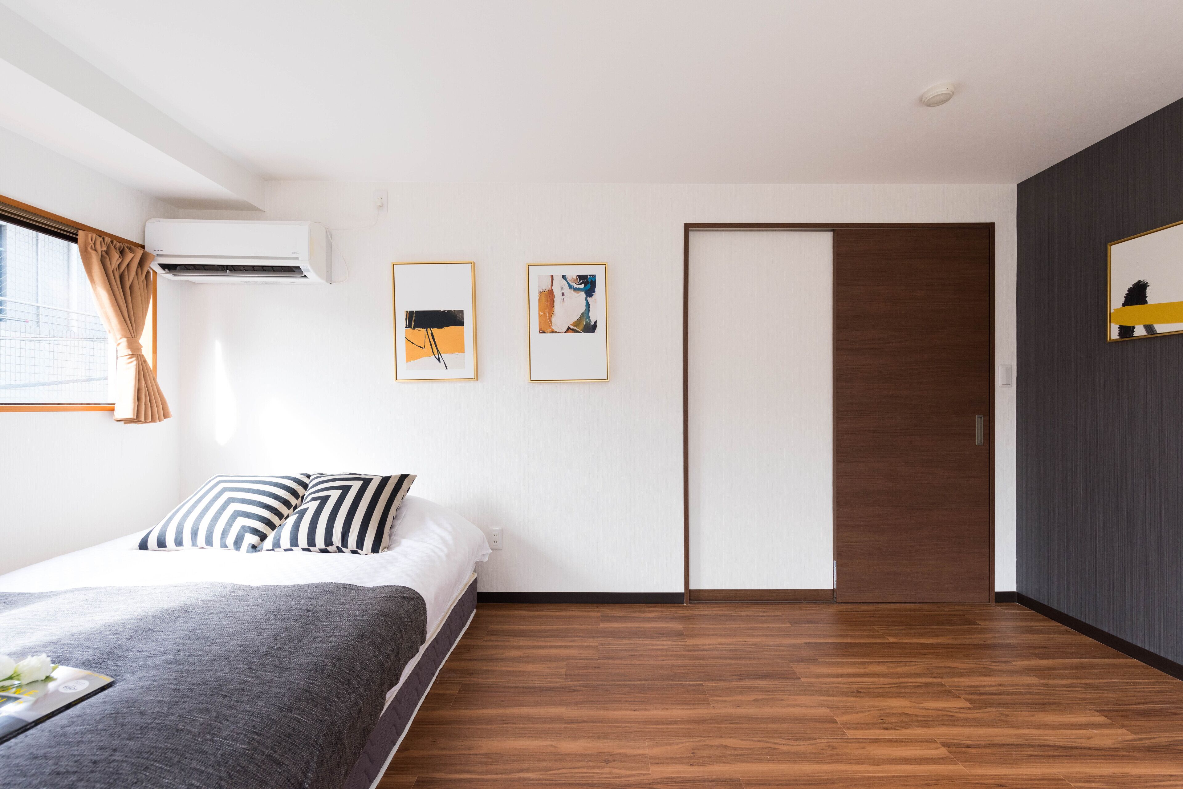 Ein modernes Schlafzimmer mit Bett, Klimaanlage, zwei gerahmten Kunstwerken, einer Schiebetür und Holzböden.