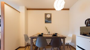 A dining area with a wooden table, four chairs, a painting on the wall, and a modern light fixture. - TORA Hotel Ueno 193D (Tokyo)