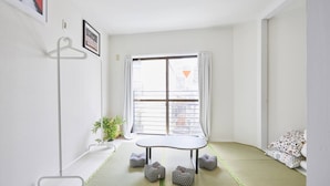 A minimalist room with tatami flooring, a tatami mat table, a hanging rack, and a window with a view of buildings. - TORA Hotel Kita Ueno144 (Tokyo)