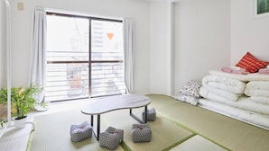 A modern living room with a large window, tatami mats, a sofa with pillows, and a small table. - TORA Hotel Kita Ueno144 (Tokyo)
