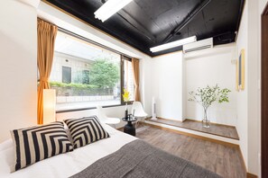 A hotel room with a bed, two chairs, a small table, a mirror, and a potted plant. - TORA HOTEL Komagome A (Tokyo)