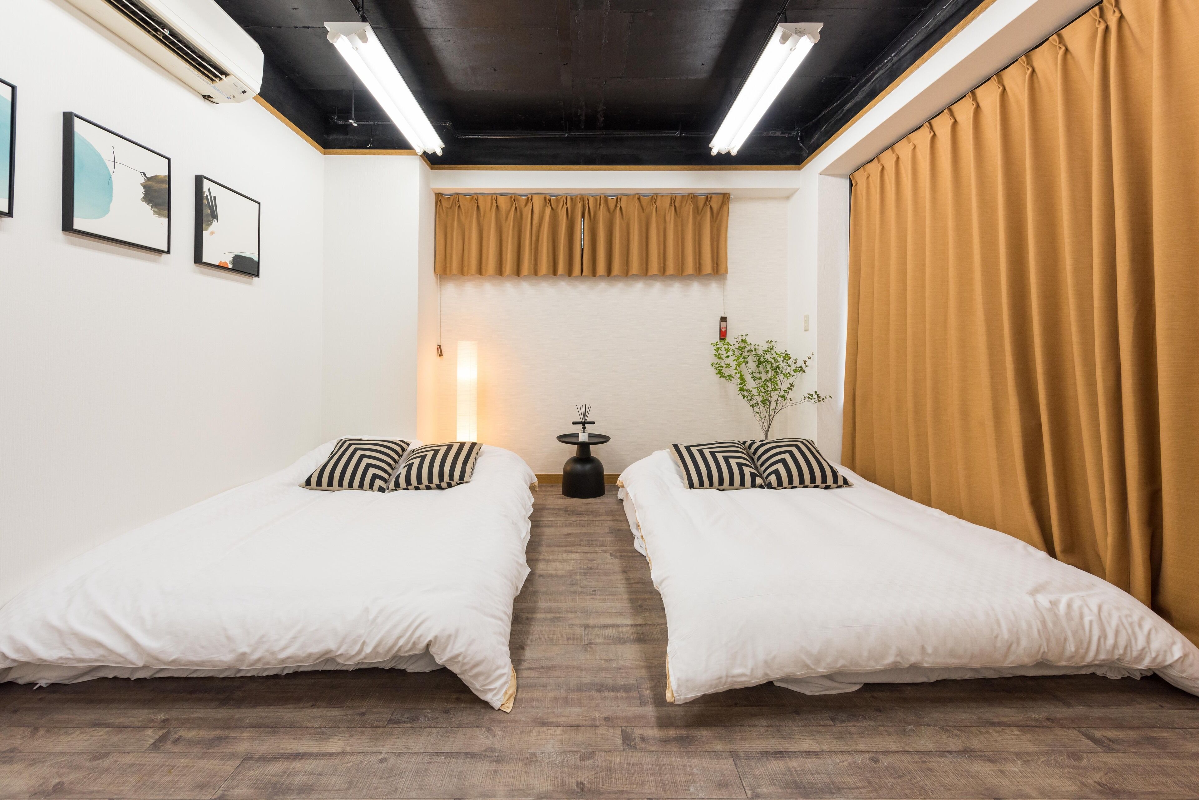 Una habitación con dos camas, una mesita, una planta y una ventana con cortinas.