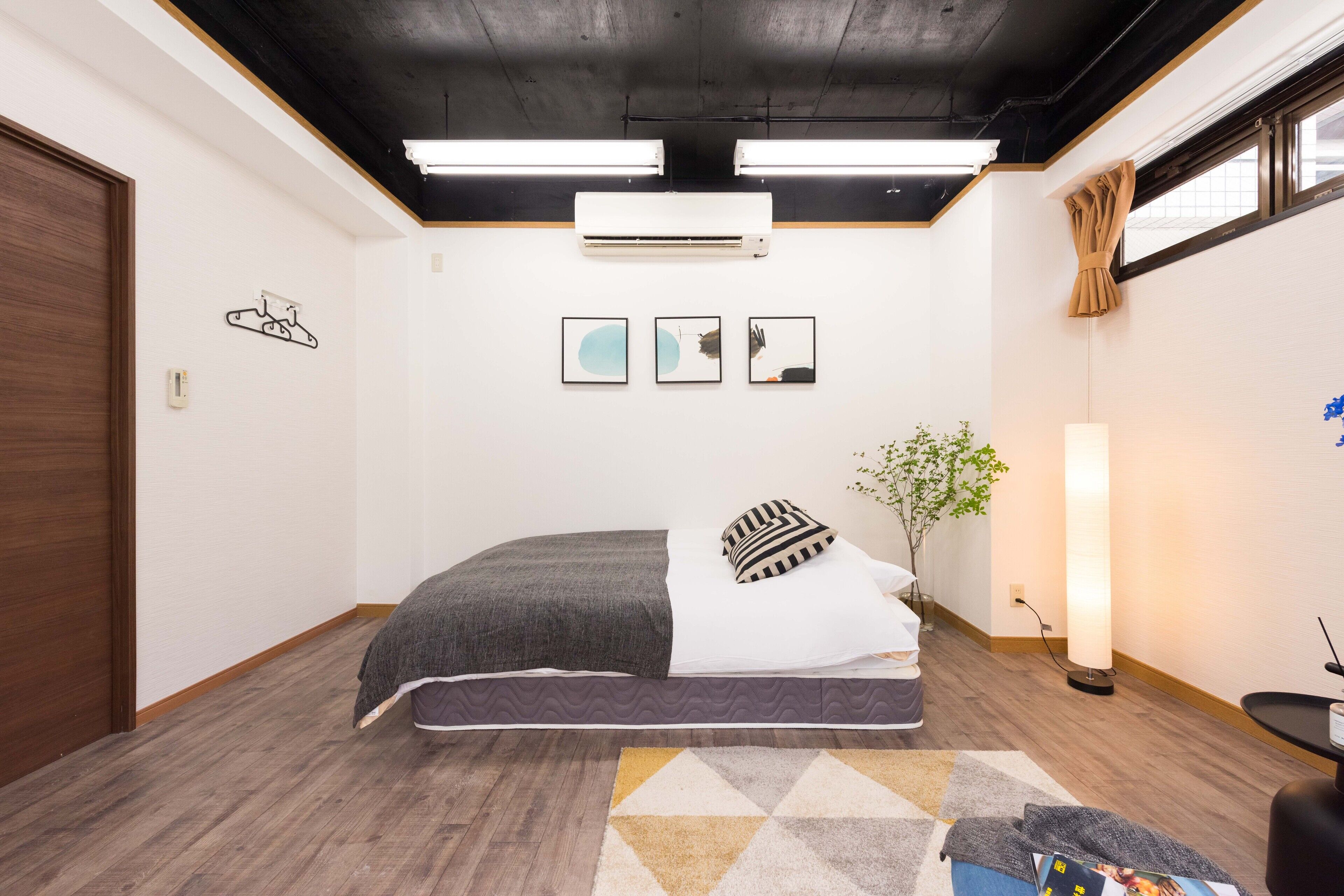 A bedroom with a bed, a wall-mounted air conditioner, a floor lamp, and a plant.