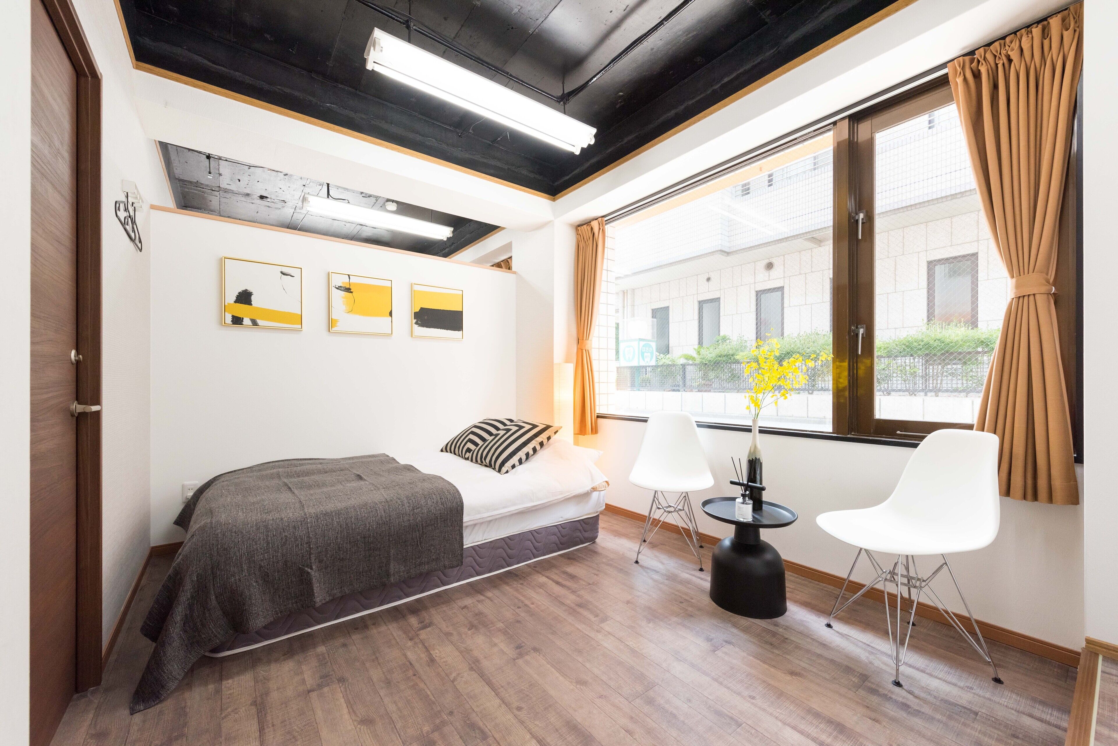 A modern bedroom with a bed, two white chairs, a small table, and artwork on the wall.