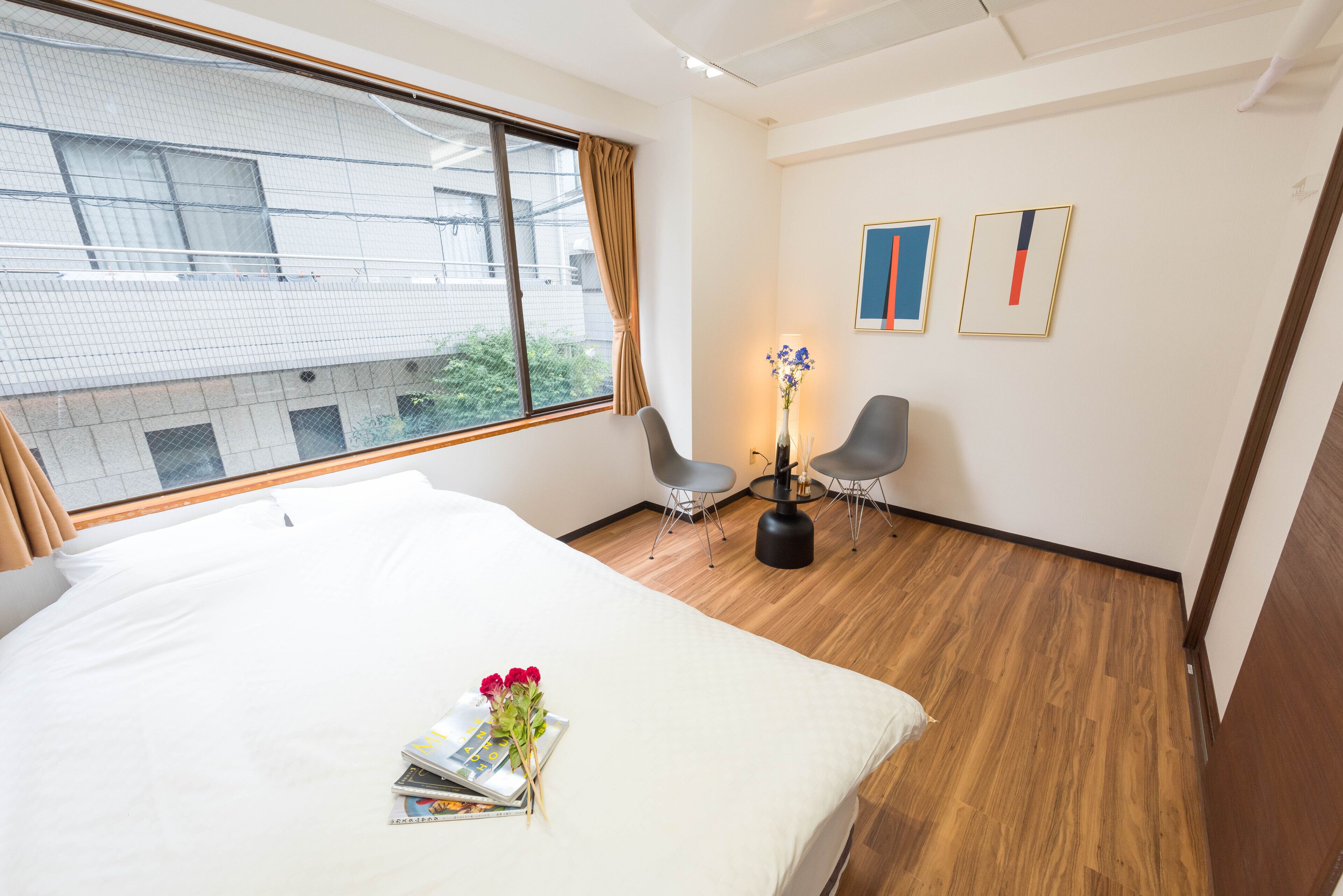 Een hotelkamer met een groot bed, een bureau met twee stoelen, een vaas met bloemen en twee kunstwerken in lijsten aan de muur.