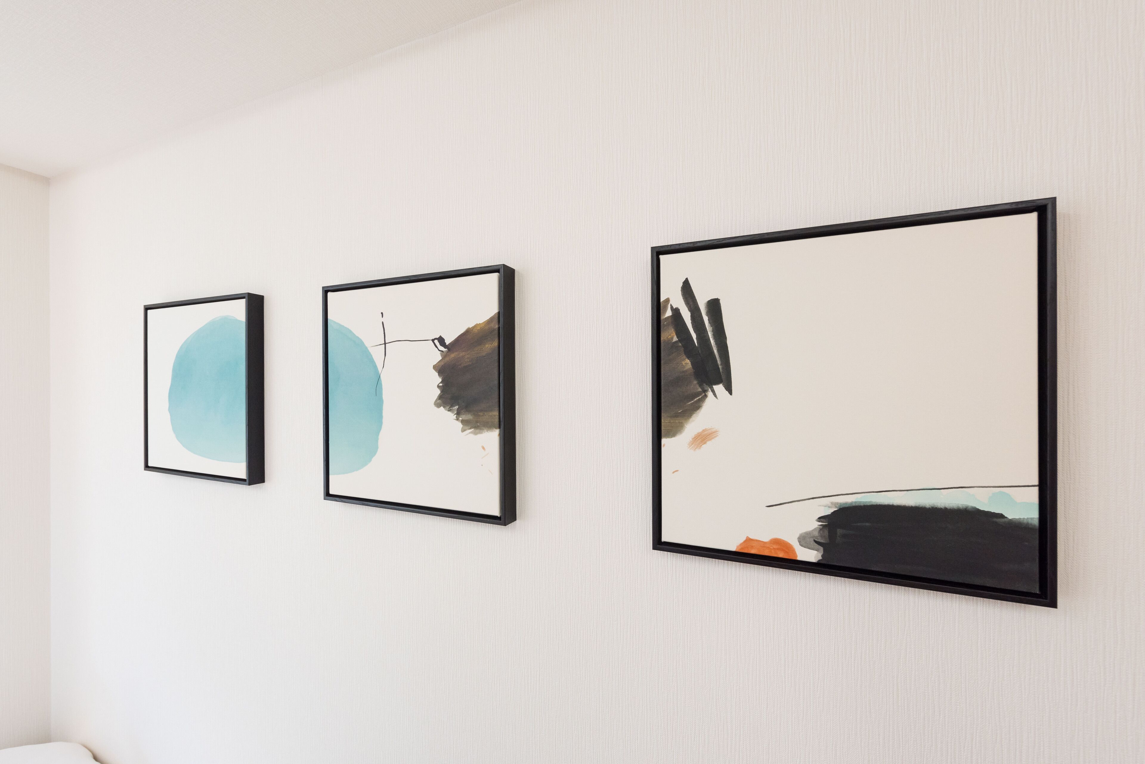 Three framed abstract paintings on a white wall.