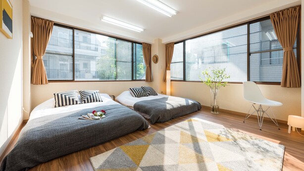 A modern hotel room with two beds, large windows, a white chair, and a geometric patterned rug. - TORA HOTEL Komagome B (Tokyo)