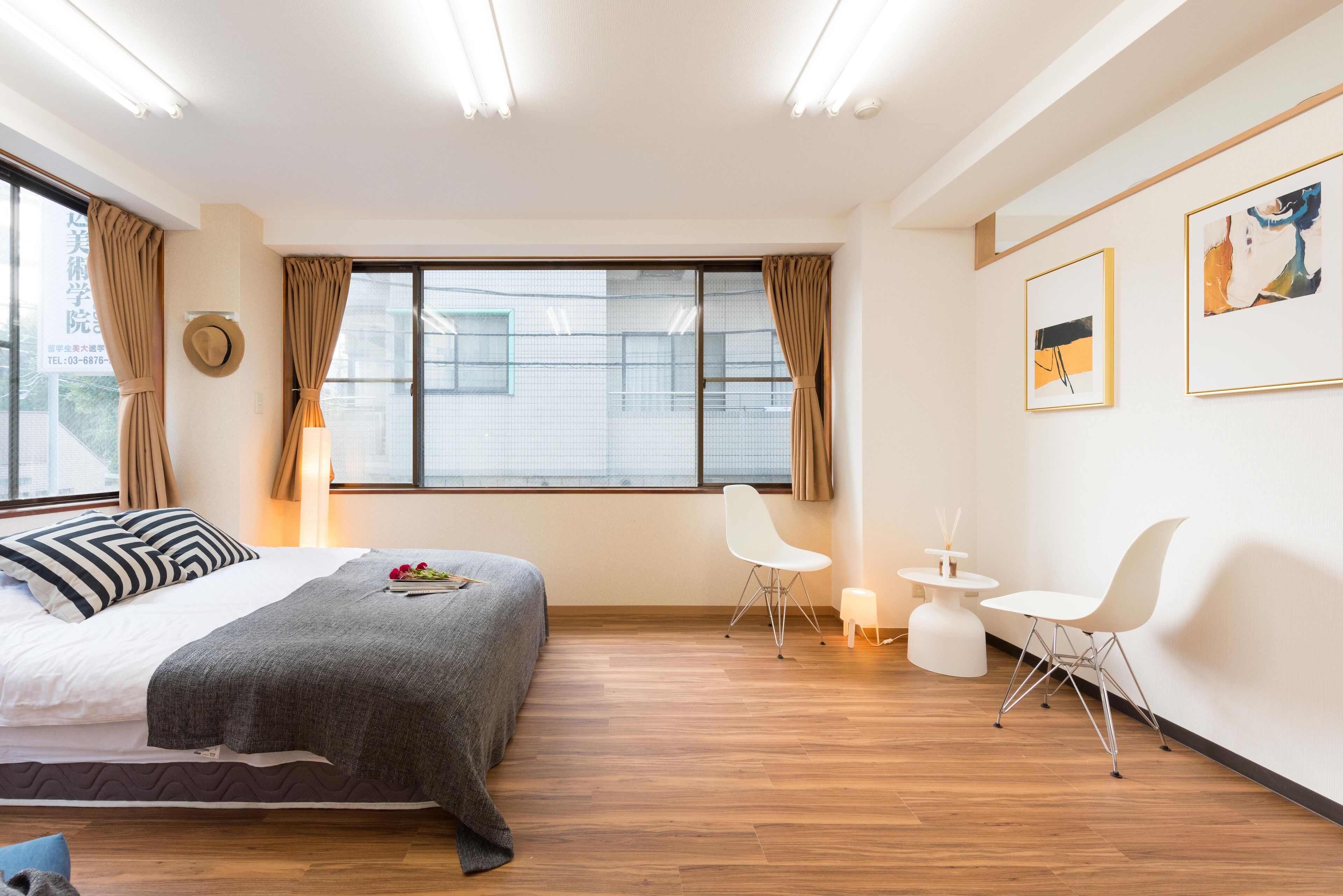Ett modernt hotellrum med en stor säng, ett litet matbord, två vita stolar, ett runt bord med ett ljus och konstverk på väggen.