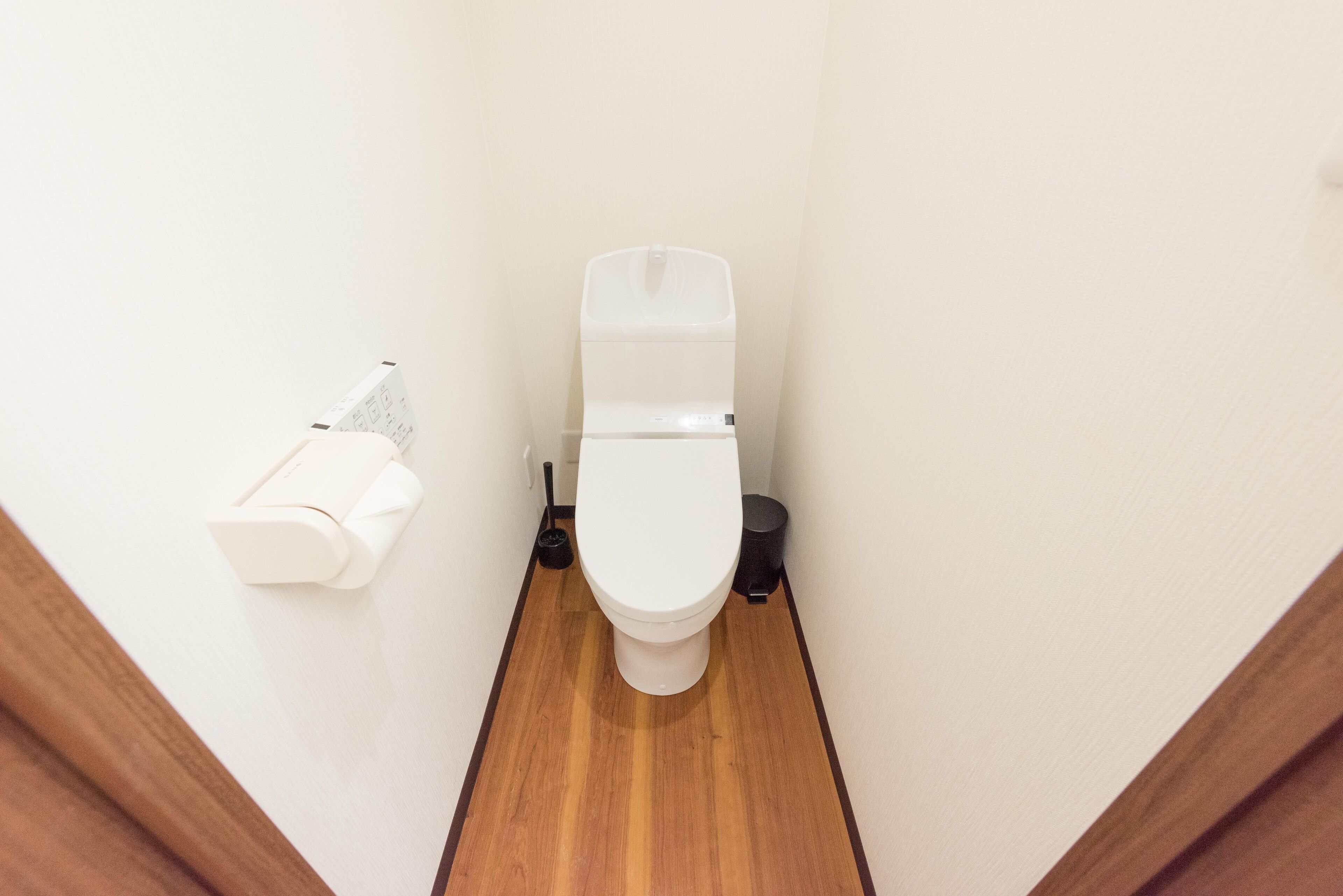 A small, narrow bathroom with a white toilet, a toilet paper holder, and a black trash bin.