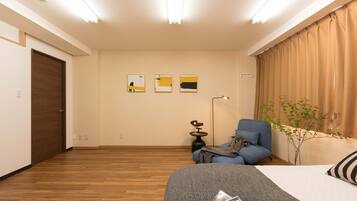 A modern hotel room with a wooden floor, a bed with a grey blanket, a blue armchair, a small side table, and three abstract wall art pieces.