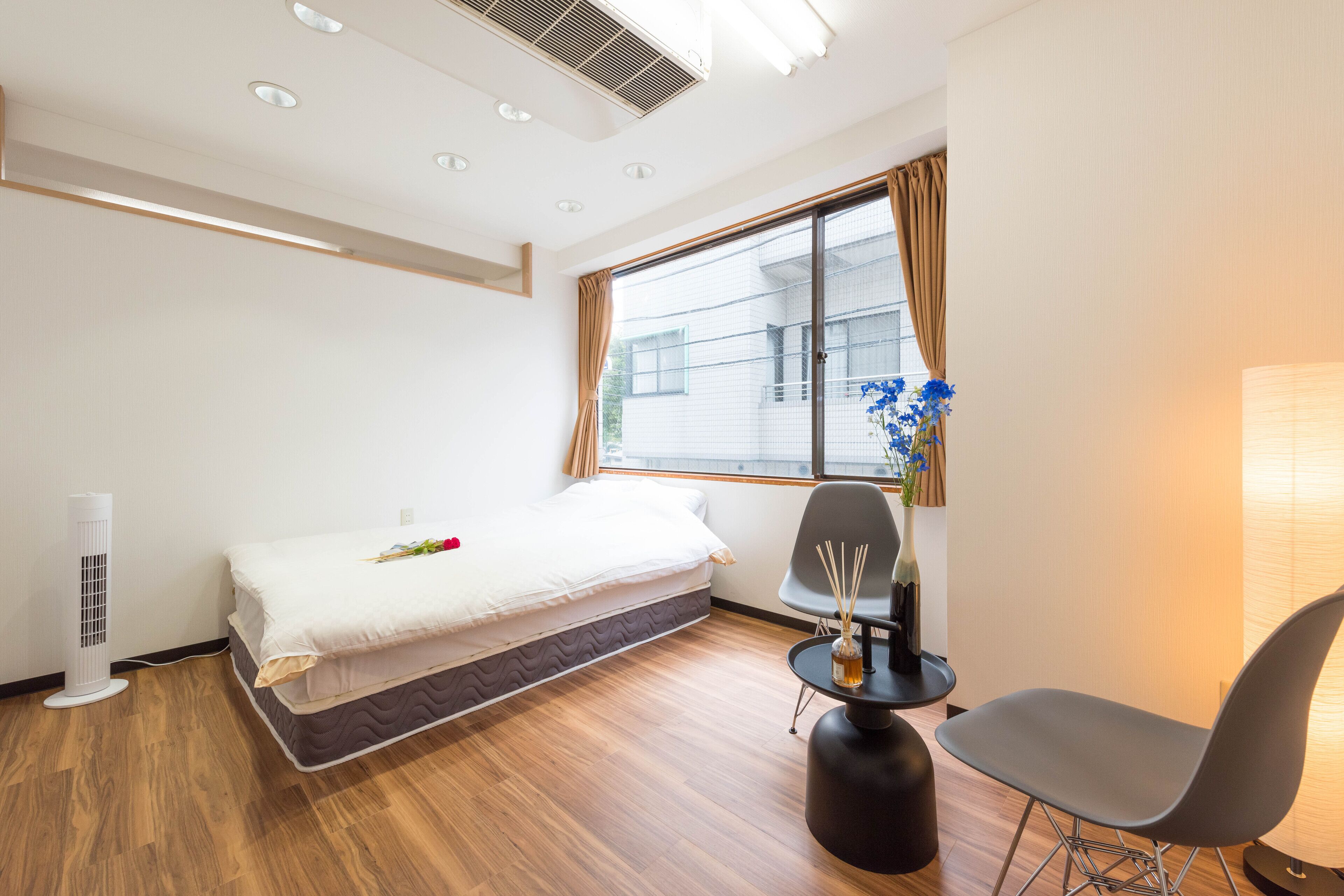 Quarto de hotel moderno com cama, cadeira, mesinha e janela com cortinas.