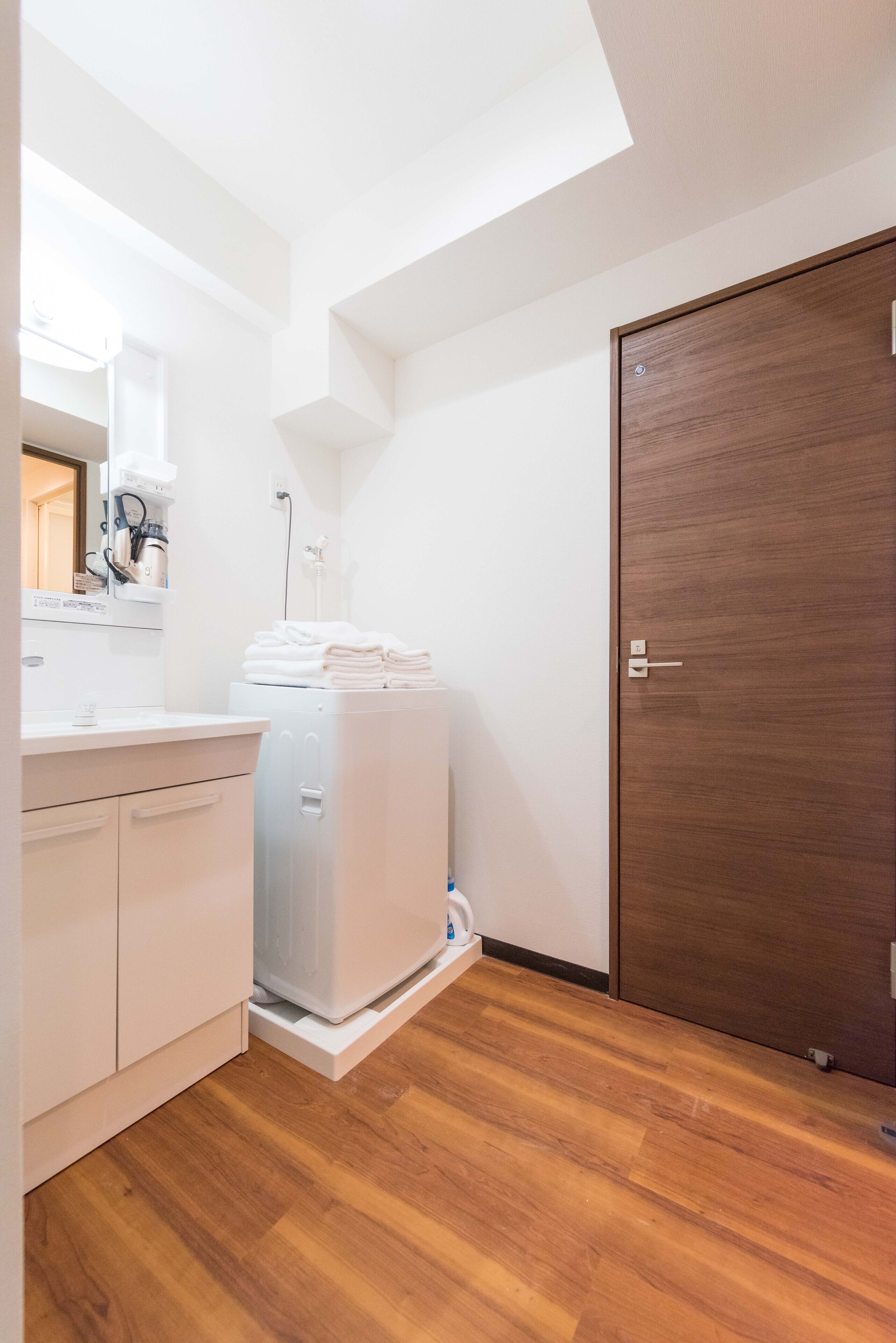 Un bagno compatto con un lavandino bianco, uno specchio e una lavatrice bianca.