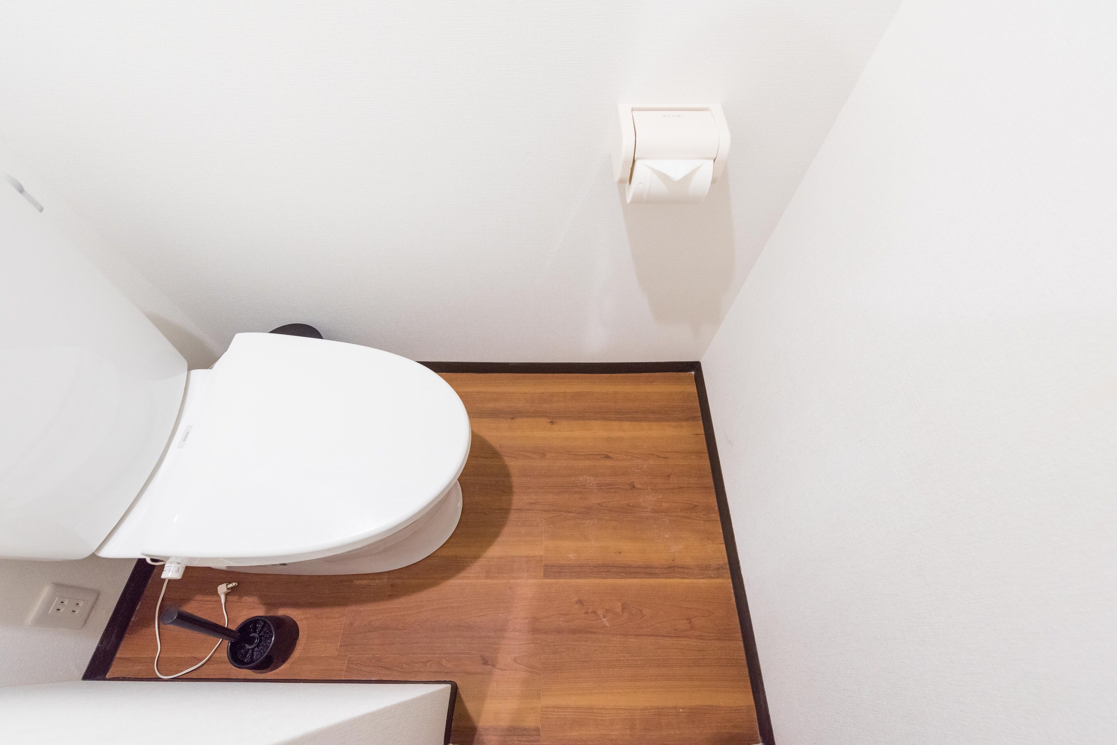 A small, clean bathroom with a white toilet, a wooden floor, and a white wall.