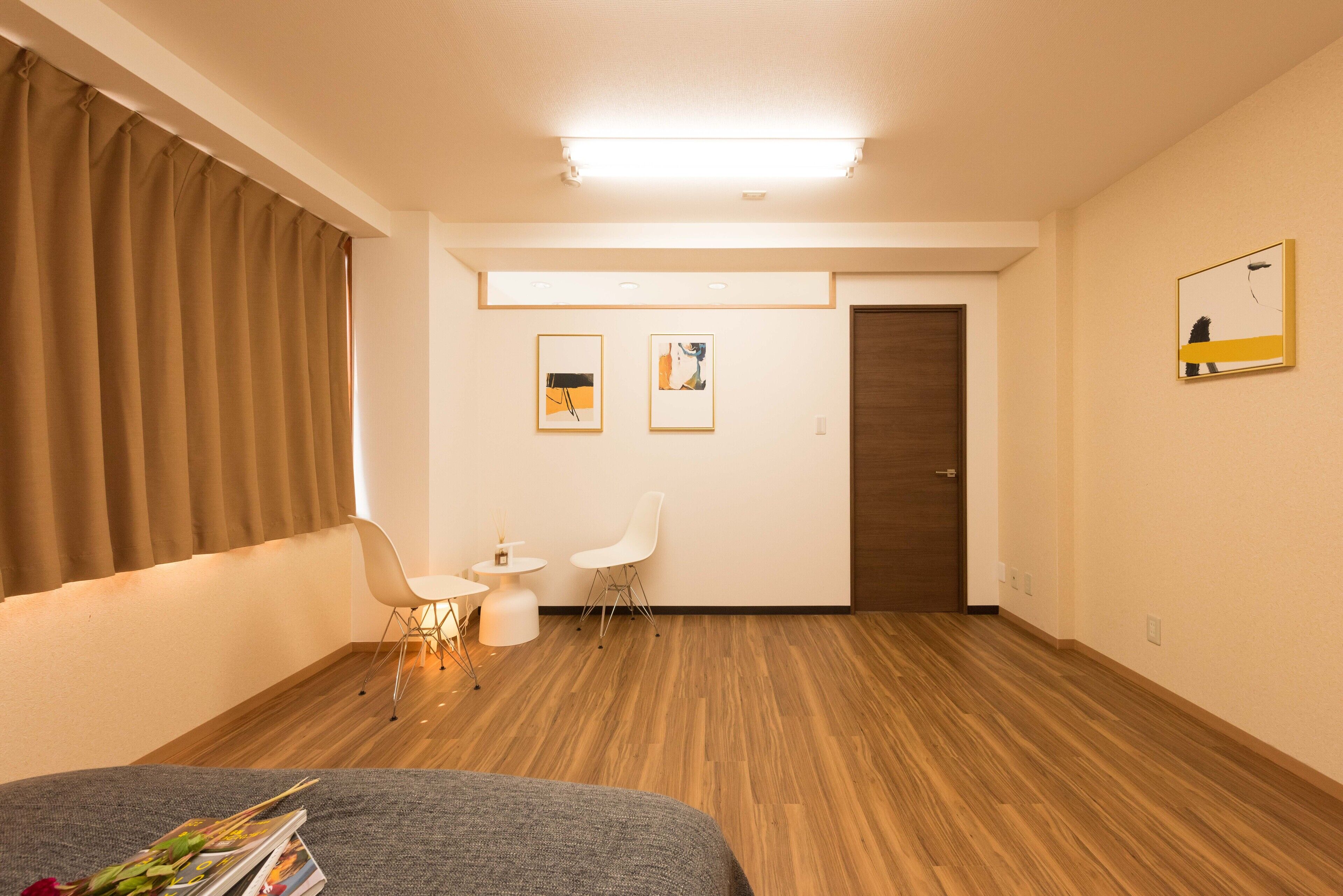 Une chambre d’hôtel moderne avec un plancher en bois, un lit, un bureau avec deux chaises et des œuvres d’art accrochées aux murs.