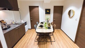 A compact kitchen with a dining area, wooden cabinets, a built-in stove, and a small refrigerator. - TORA HOTEL Komagome B (Tokyo)