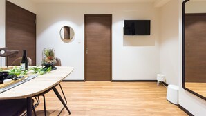 A modern room with a wooden floor, a dining table with a bottle and a plant, a mirror, and a TV mounted on the wall. - TORA HOTEL Komagome B (Tokyo)