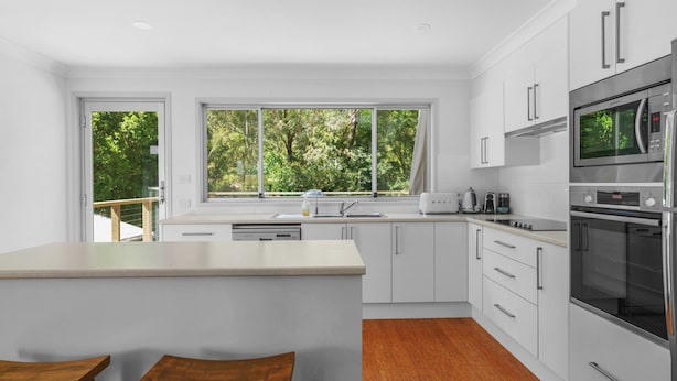 A modern kitchen with white cabinetry, a large window, and a built-in oven. - Elaine at Hyams Beach, Jervis Bay (Hyams Beach)
