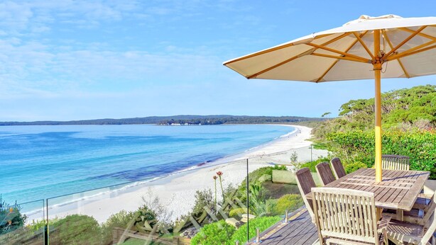 Eine Terrasse direkt am Strand mit einem Holztisch und Stühlen, einem Sonnenschirm und Blick auf den Ozean und den Strand.